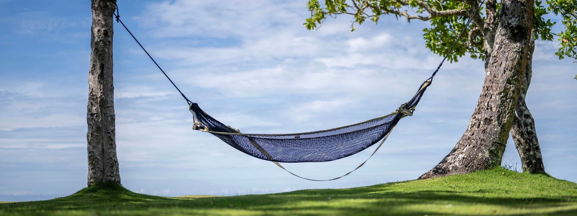 Beach hammock tied between trees on grassy area under blue sky at The Naviti Resort in Korolevu