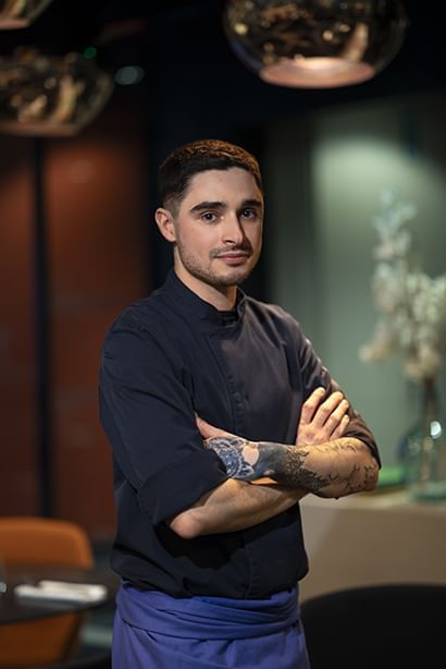 Un chef en costume noir posant pour une photo à l'Oceania Paris Roissy CDG