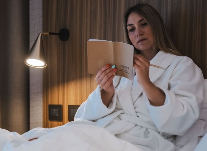 Donna in accappatoio su letto legge opuscolo al DUPARC
