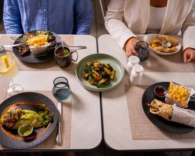 Couple dining with a steak plate and chicken wrap beside a fresh green salad bowl at Sugar Cane Club Hotel & Spa resort