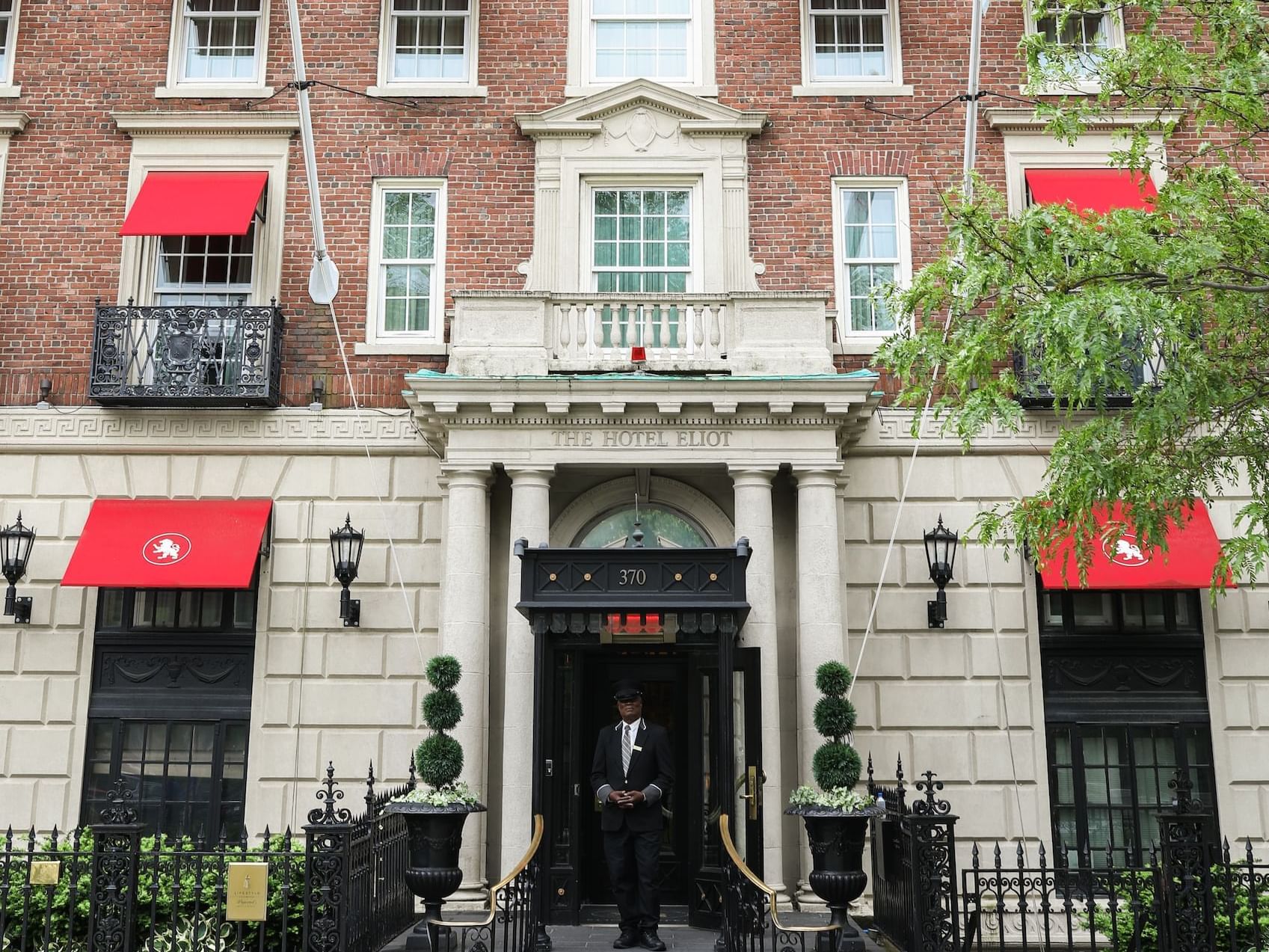 A doorman in a black uniform standing in front of a brick and stone building.