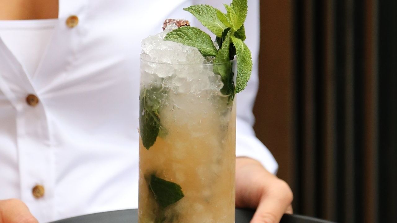 Close-up of a waitress serving a cocktail mojito tamarind glass in a restaurant at Warwick Le Crystal