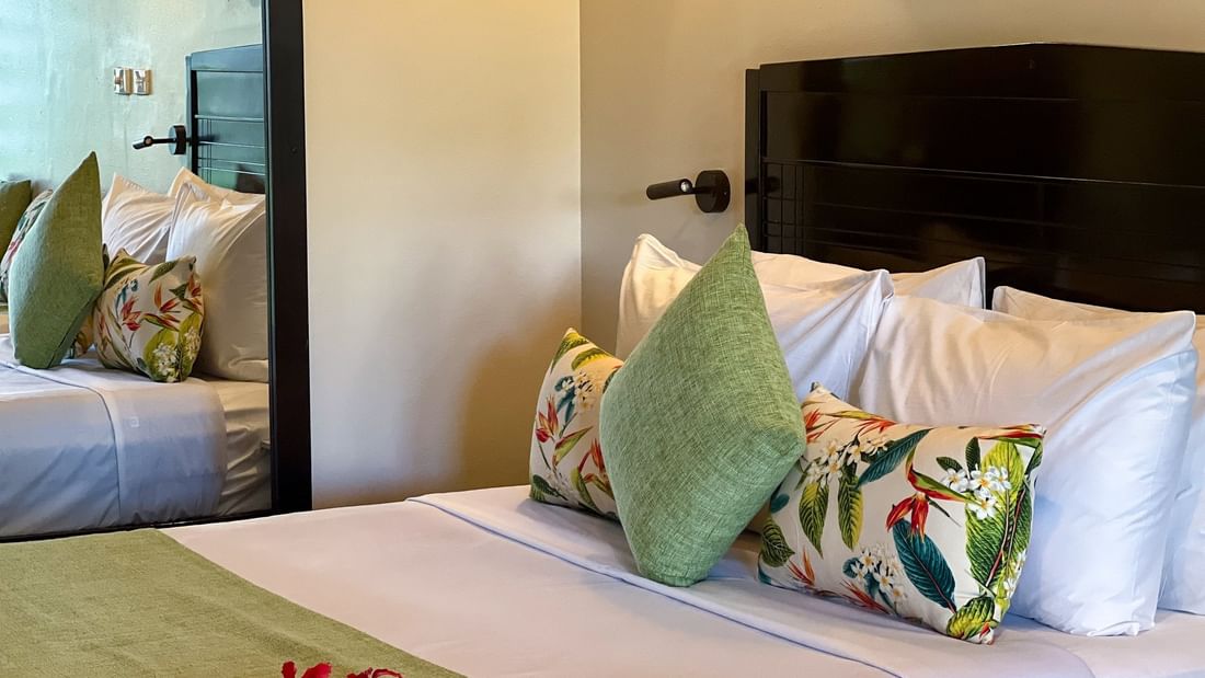 White bed with green pillows by a large mirror under a black headboard in Deluxe Villa at Warwick Hotels & Resorts