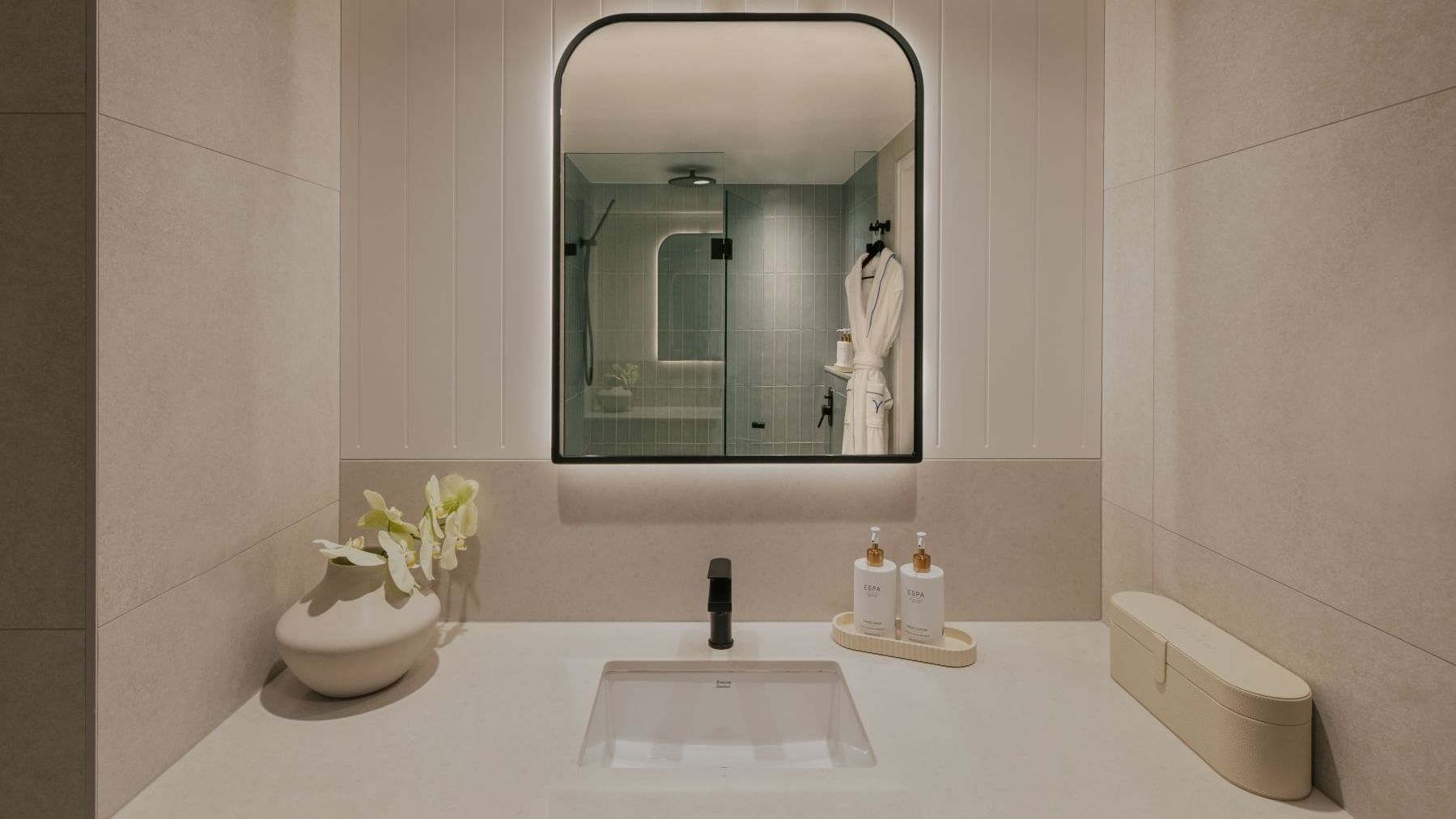 Ocean View King – Elysium Floor at Elysium Manly, featuring a sink with lotion bottles under a lit mirror, next to a vase