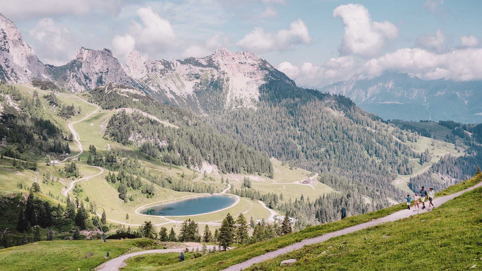 Scenic view of mountains with a lake and hikers on a trail near Falkensteiner Hotel Sonnenalpe