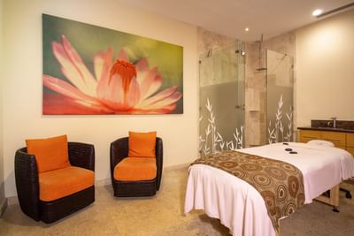 Sala del Zenset Spa con mesa de masaje, sillas de mimbre, ducha de cristal y una gran obra de arte en la pared en el Sunset Plaza Beach Resort