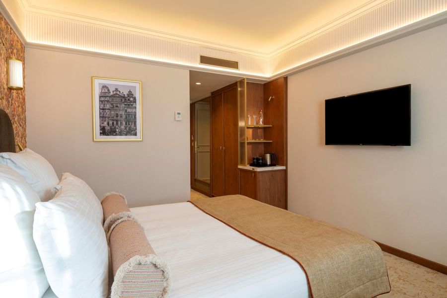 Modern hotel room with white bedding, wall-mounted TV, wooden cabinetry, and framed artwork at Warwick Brussels Grand-Place