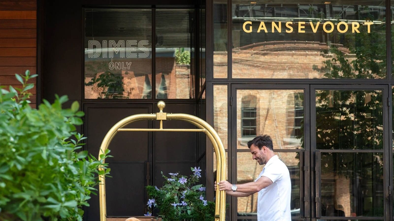 Golden retriever beside a luggage cart with greenery outside the main Gansevoort Meatpacking NYC entrance during the daytime