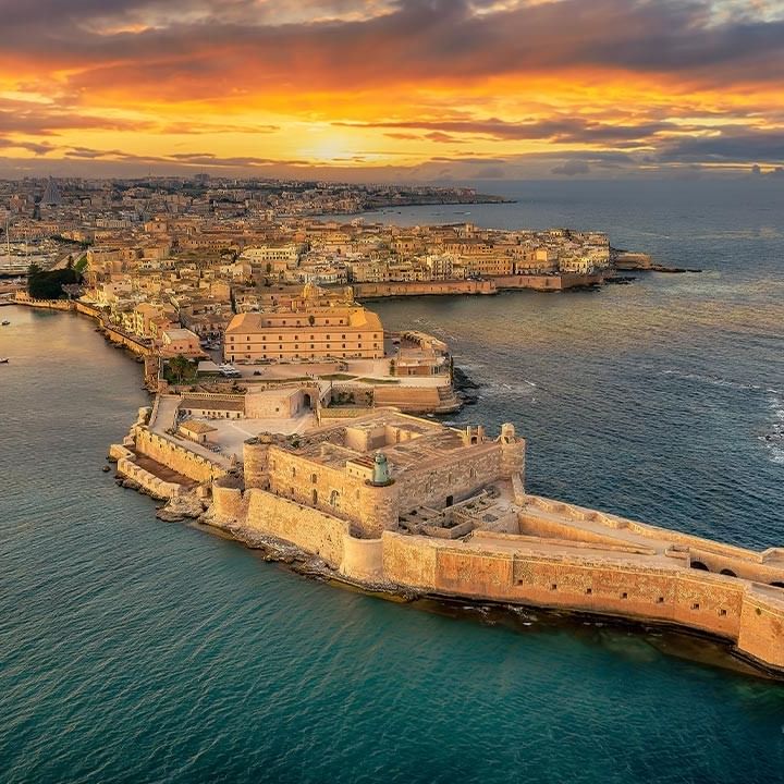 Luftaufnahme der maltesischen Küste bei Sonnenuntergang mit Festung und Stadt im Hintergrund.