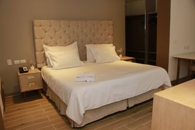 Cama de matrimonio bien equipada con cabecero empenachado y suelos de madera en una suite del Country International Hotel.