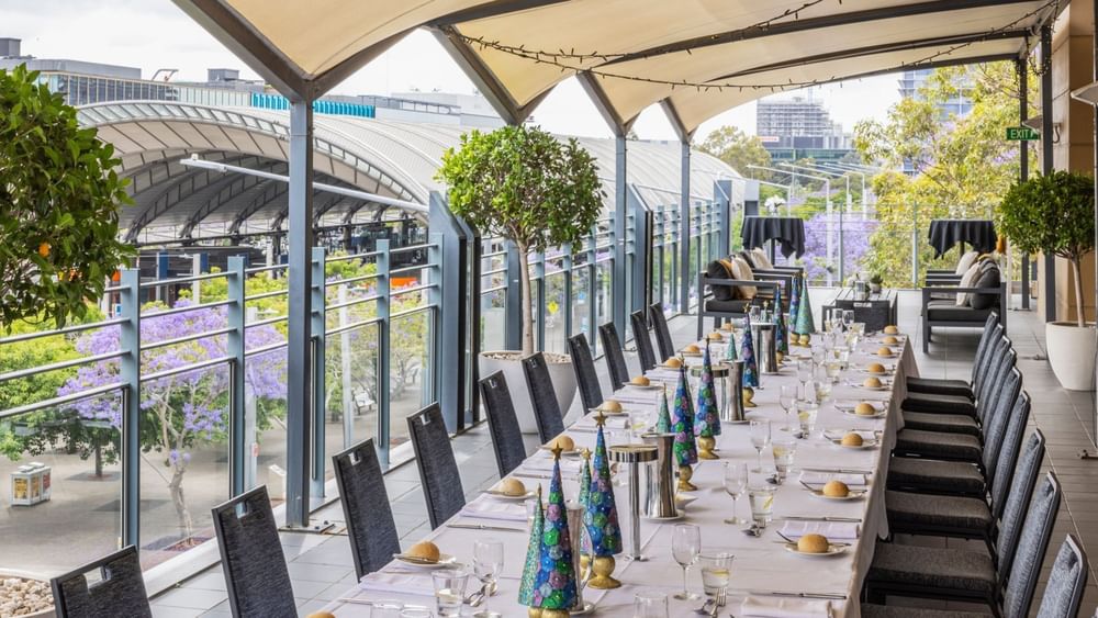 Elegant covered terrace with long banquet table set for Christmas celebration featuring festive decorations and city views
