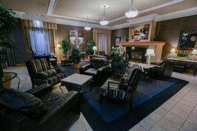 Lobby lounge with leather chairs by a stone fireplace, under pendant lights, surrounded by plants at The Glenmore Inn