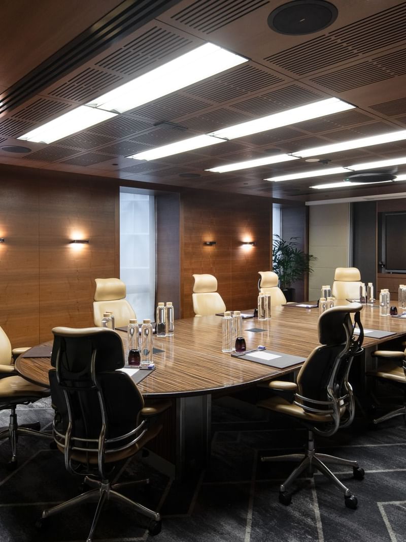 Spacious executive boardroom with a long wooden table, ergonomic chairs, and modern lighting, ideal for professional meetings.