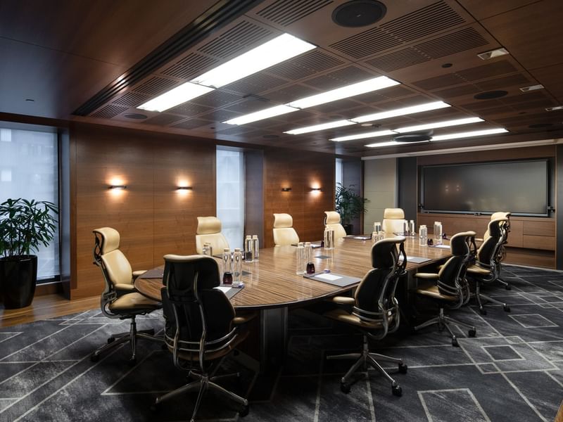 Spacious executive boardroom with a long wooden table, ergonomic chairs, and modern lighting, ideal for professional meetings.