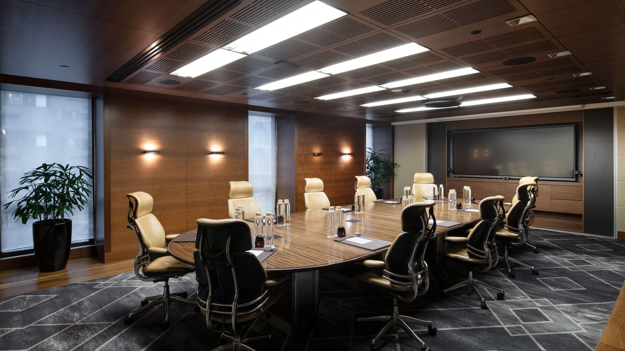 Spacious executive boardroom with a long wooden table, ergonomic chairs, and modern lighting, ideal for professional meetings.