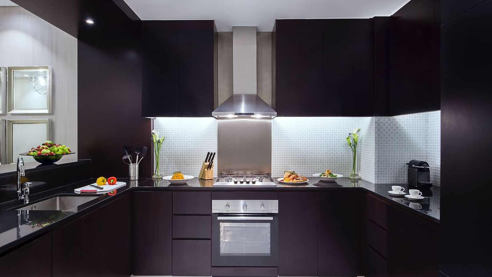 Kitchenette with black cabinets and stainless steel appliances in One Bedroom Suite at DAMAC Maison Distinction