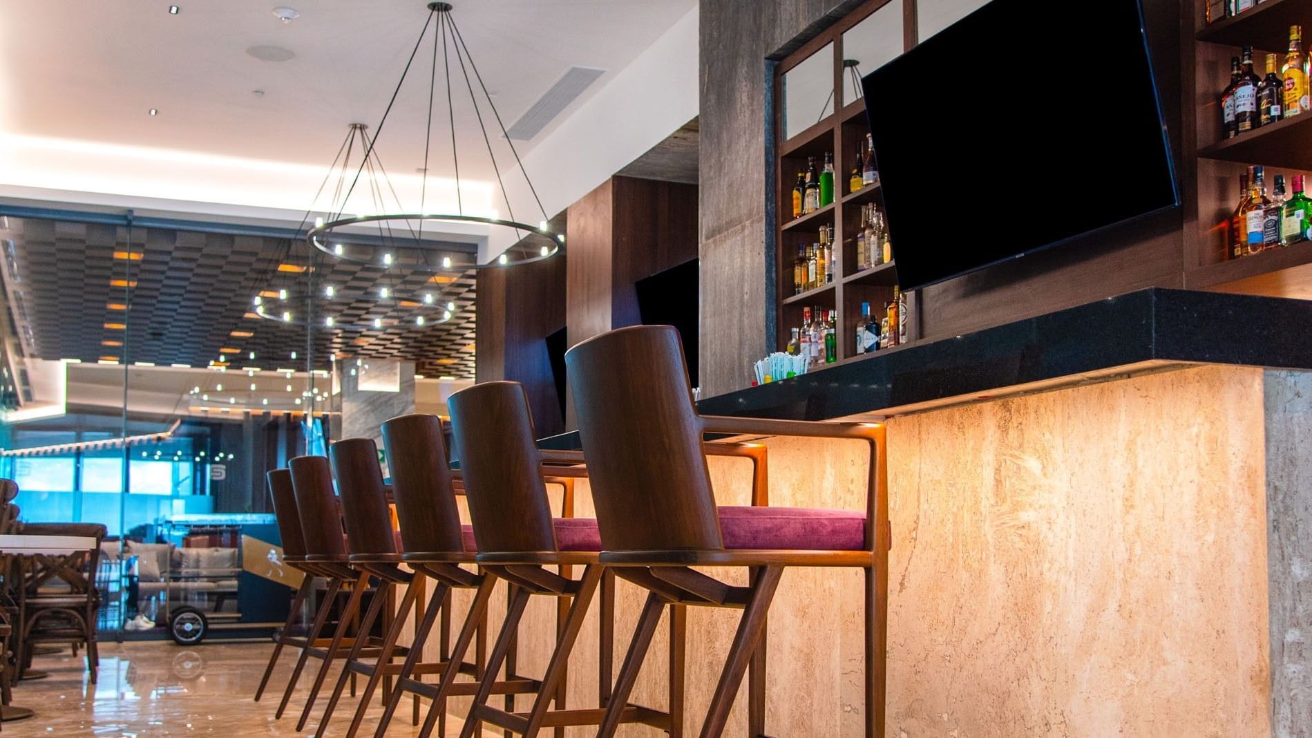 Upscale Lobby Bar with high wooden stools, a marble counter, and modern chandeliers at Camino Real Merida