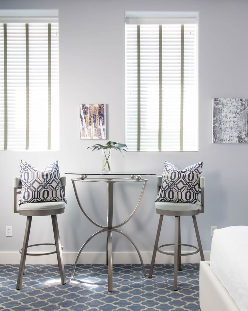 a table with two high chairs with pillows between two windows