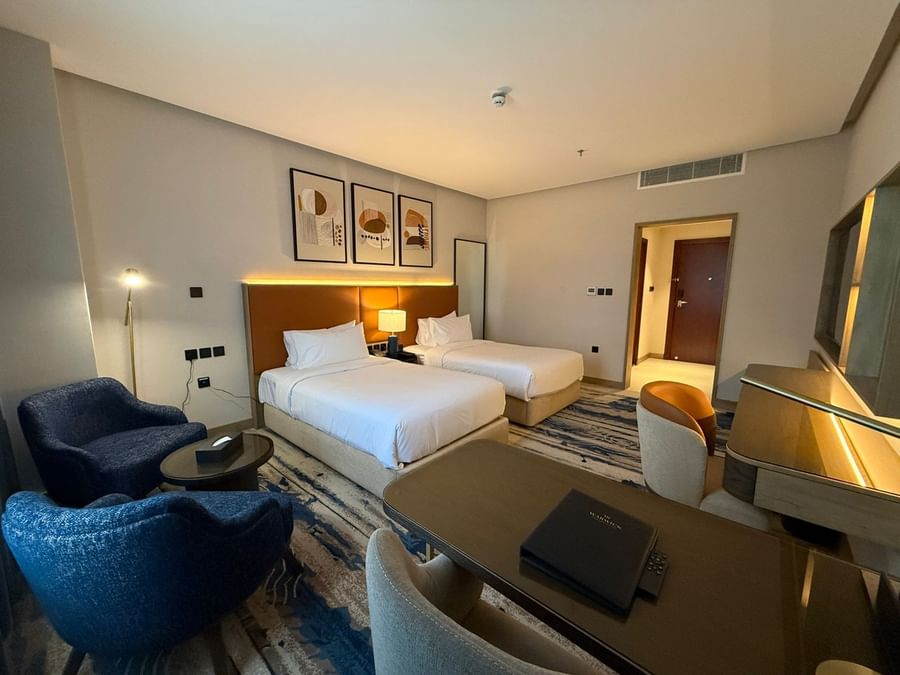 Two beds under hanging wall arts, with a couch near the working desk in Standard Room at Warwick Jeddah Hotel & Spa