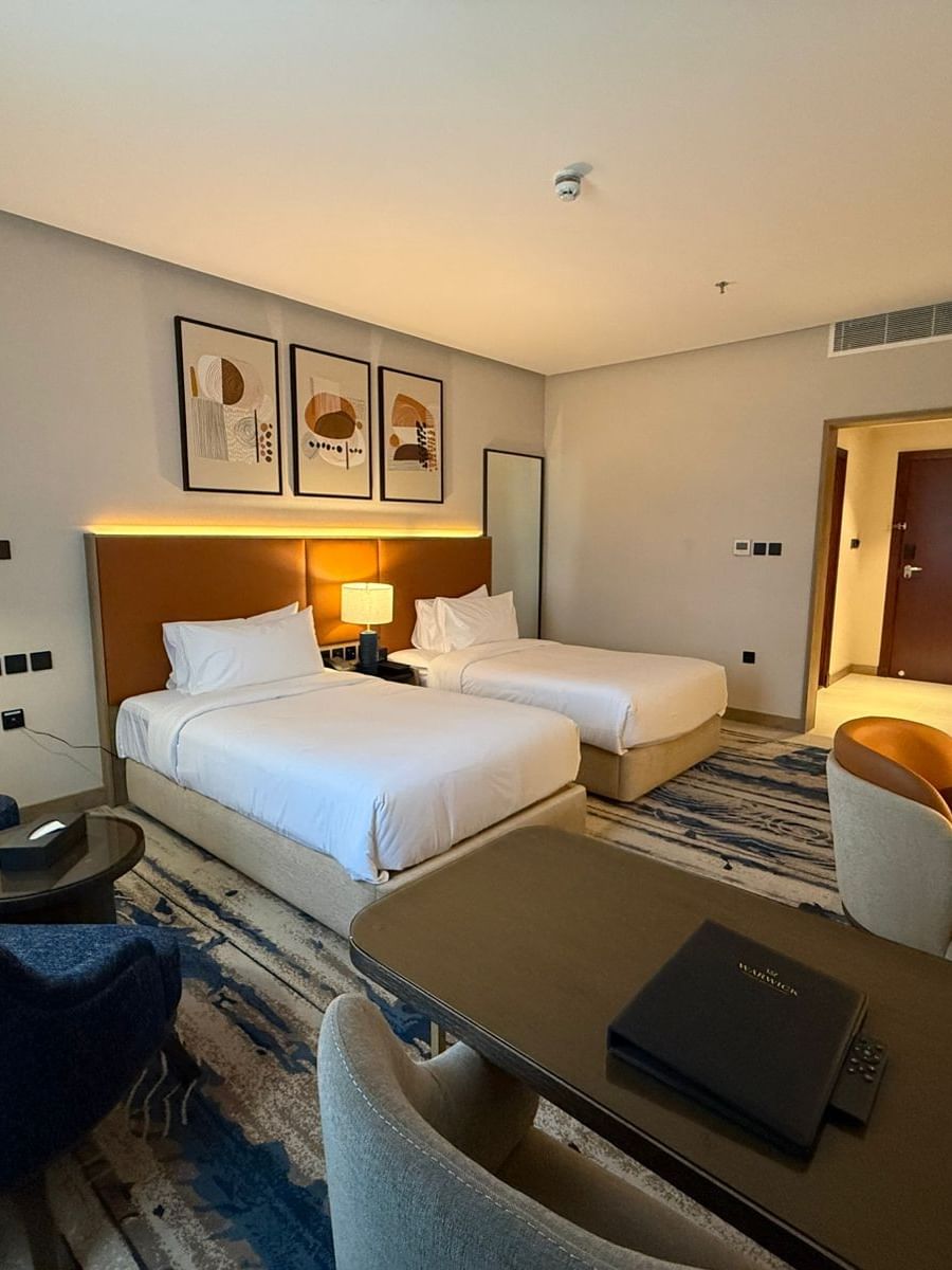 Two beds under hanging wall arts, with a couch near the working desk in Standard Room at Warwick Jeddah Hotel & Spa