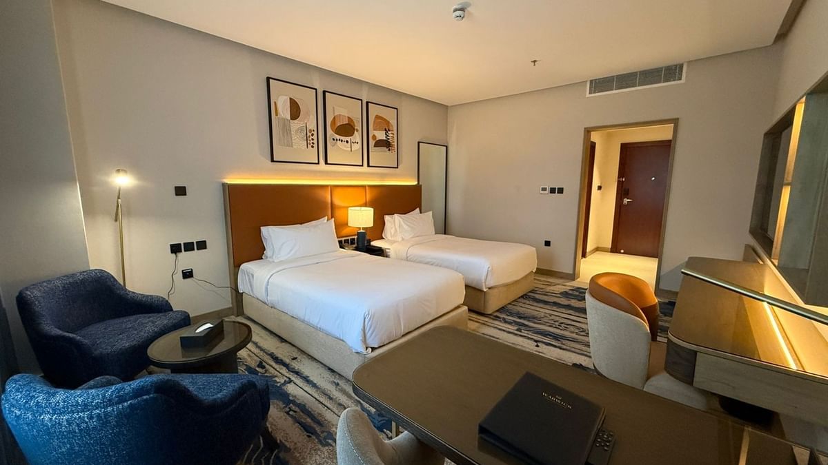 Two beds under hanging wall arts, with a couch near the working desk in Deluxe Room at Warwick Jeddah Hotel & Spa 