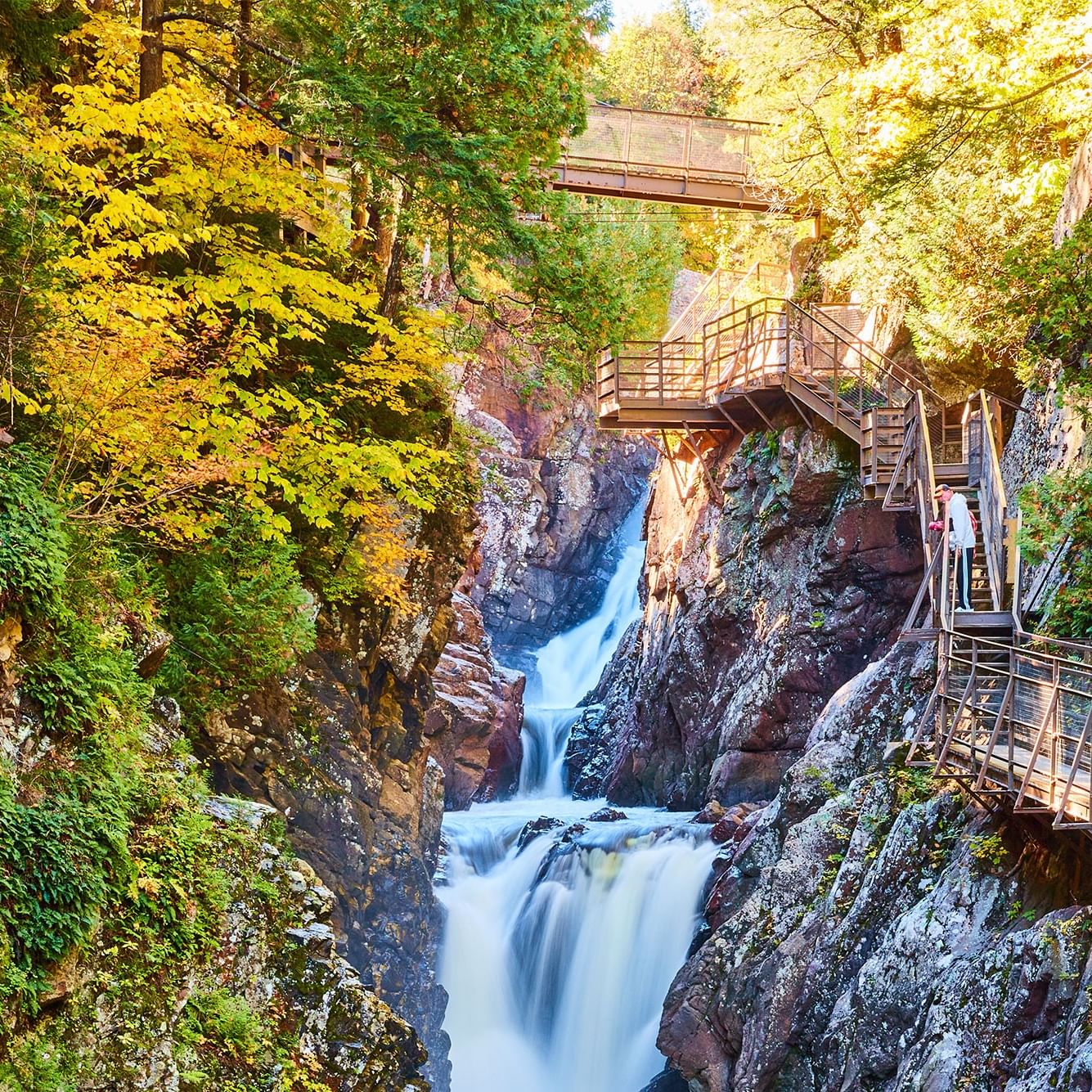 Waterfall flowing through a rocky gorge with a metal bridge and staircase on the right side.