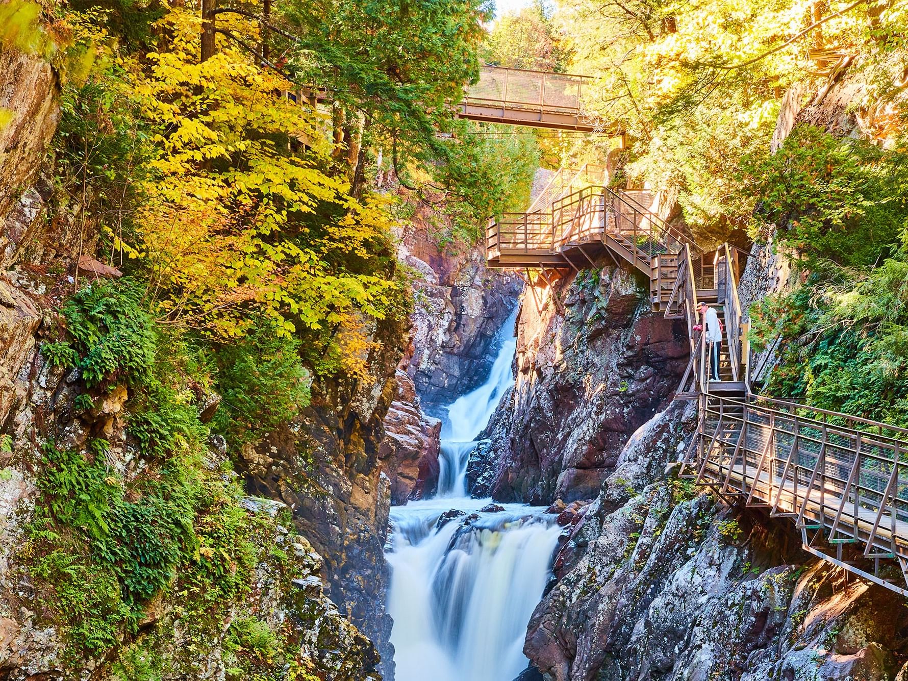 Waterfall flowing through a rocky gorge with a metal bridge and staircase on the right side near High Peaks Resort