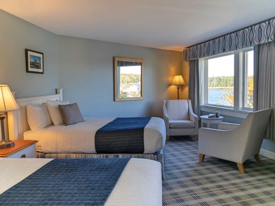 Two cozy beds, nightstand and sitting area in Lighthouse Double Beds at Sebasco Harbor Resort by Ogunquit Collection