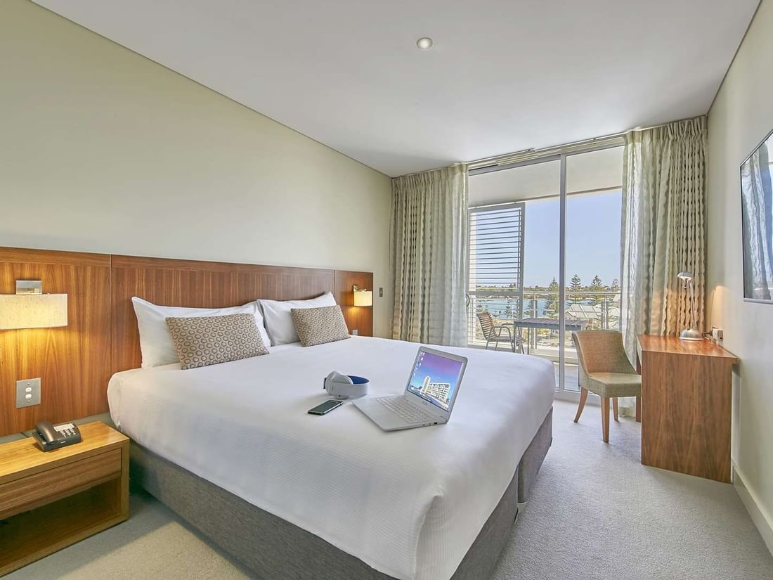 Modern Interconnecting Apartment room at The Sebel Mandurah, well-lit with a large bed and a desk with a laptop