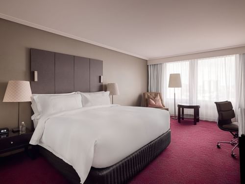 Sofitel Brisbane Central Superior Room with a large bed, bedside lamps, armchair, desk, and sheer curtained window