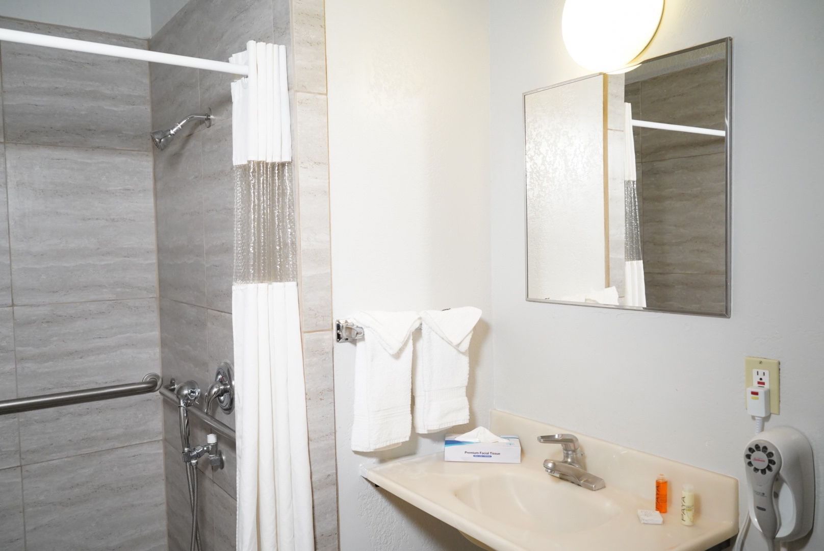 A standard hotel bathroom with a shower, sink, and mirror