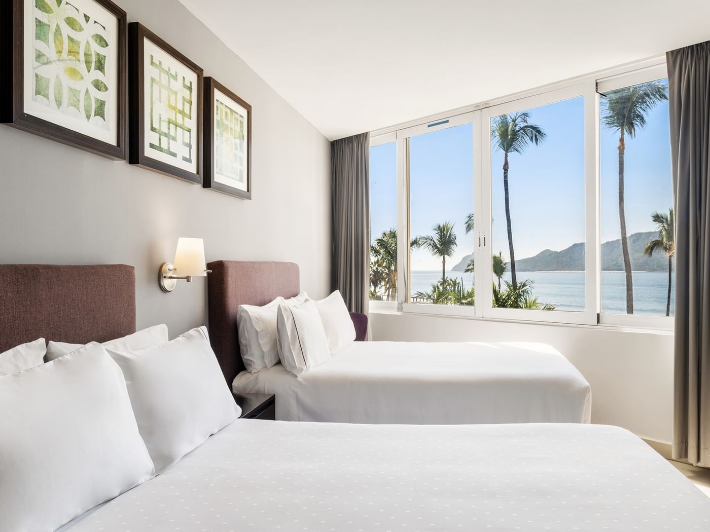 Junior Suite Vista Al Mar room with two cozy beds and large windows overlooking a tropical beach at Sunvivia Mazatlán