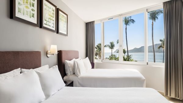 Junior Suite Vista Al Mar room with two cozy beds and large windows overlooking a tropical beach at Sunvivia Mazatlán