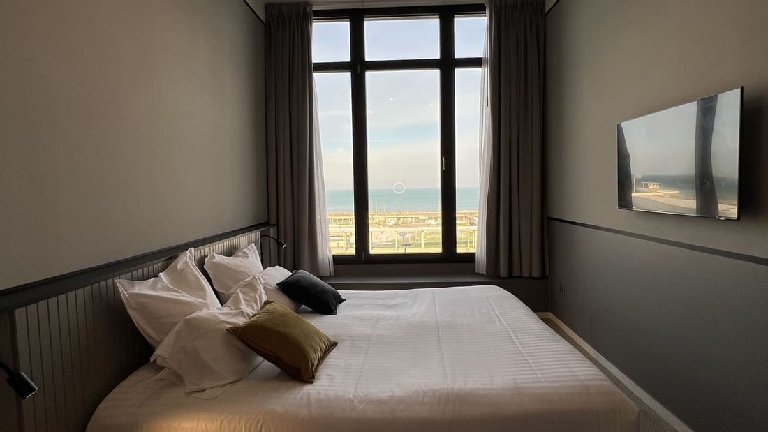 Chambre avec lit, fenêtre vue mer, lustre, et TV murale.