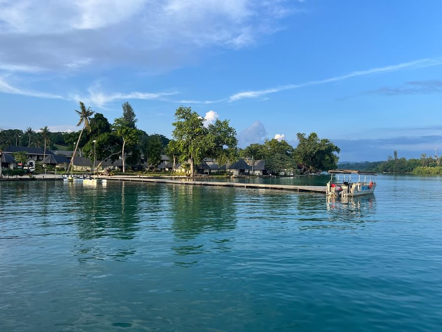 Docked boat on calm waters with lush greenery and cottages in the background.