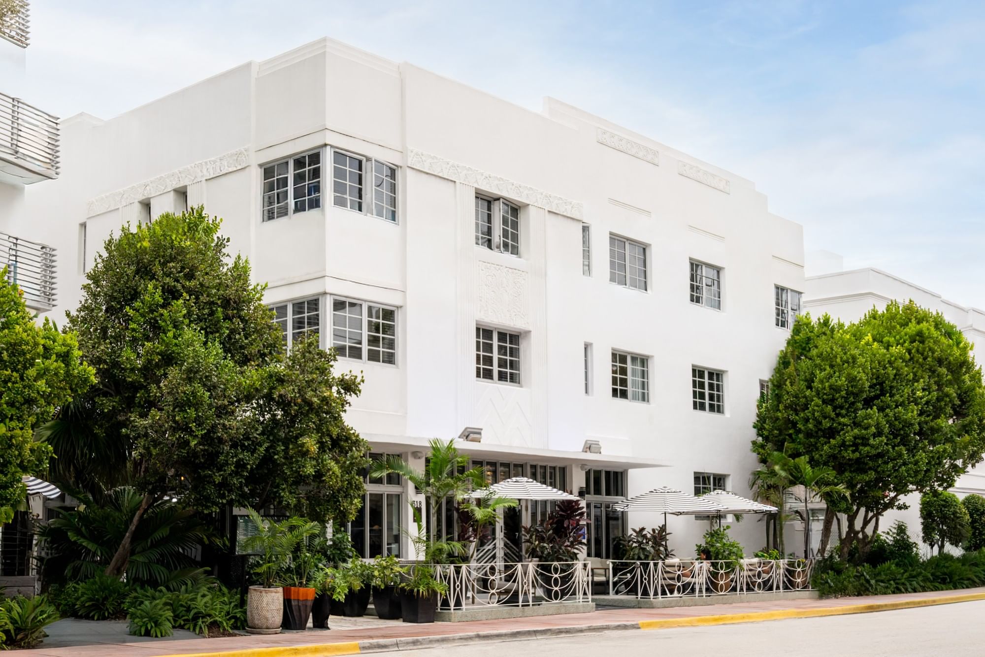 A white three-story building with balconies and trees in front of it.
