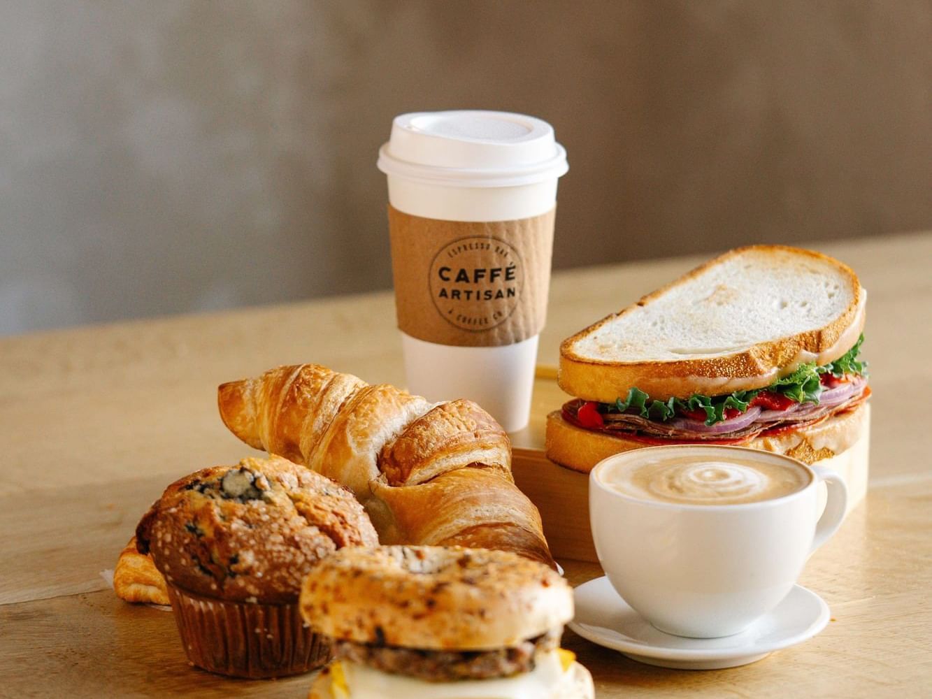 Coffee, muffin, croissant, sandwich, and a latte on a table.