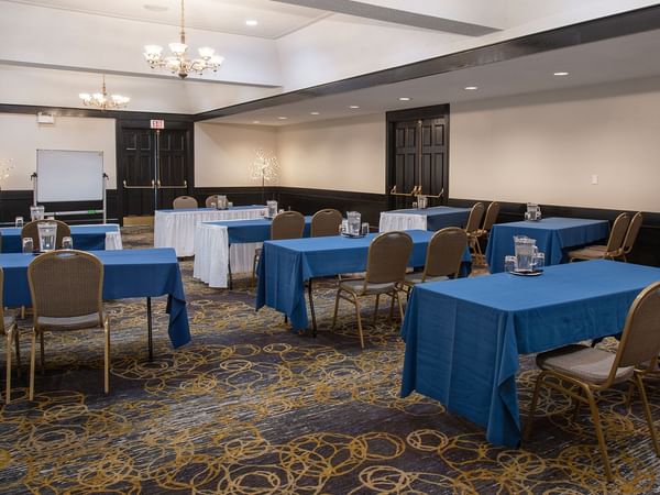 Conference room with tables, chairs, and a whiteboard, lit by chandeliers.