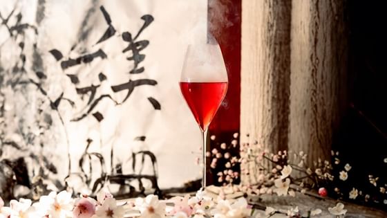 A glass of red drink surrounded by flowers and a backdrop of Asian calligraphy artwork at The Kitchens