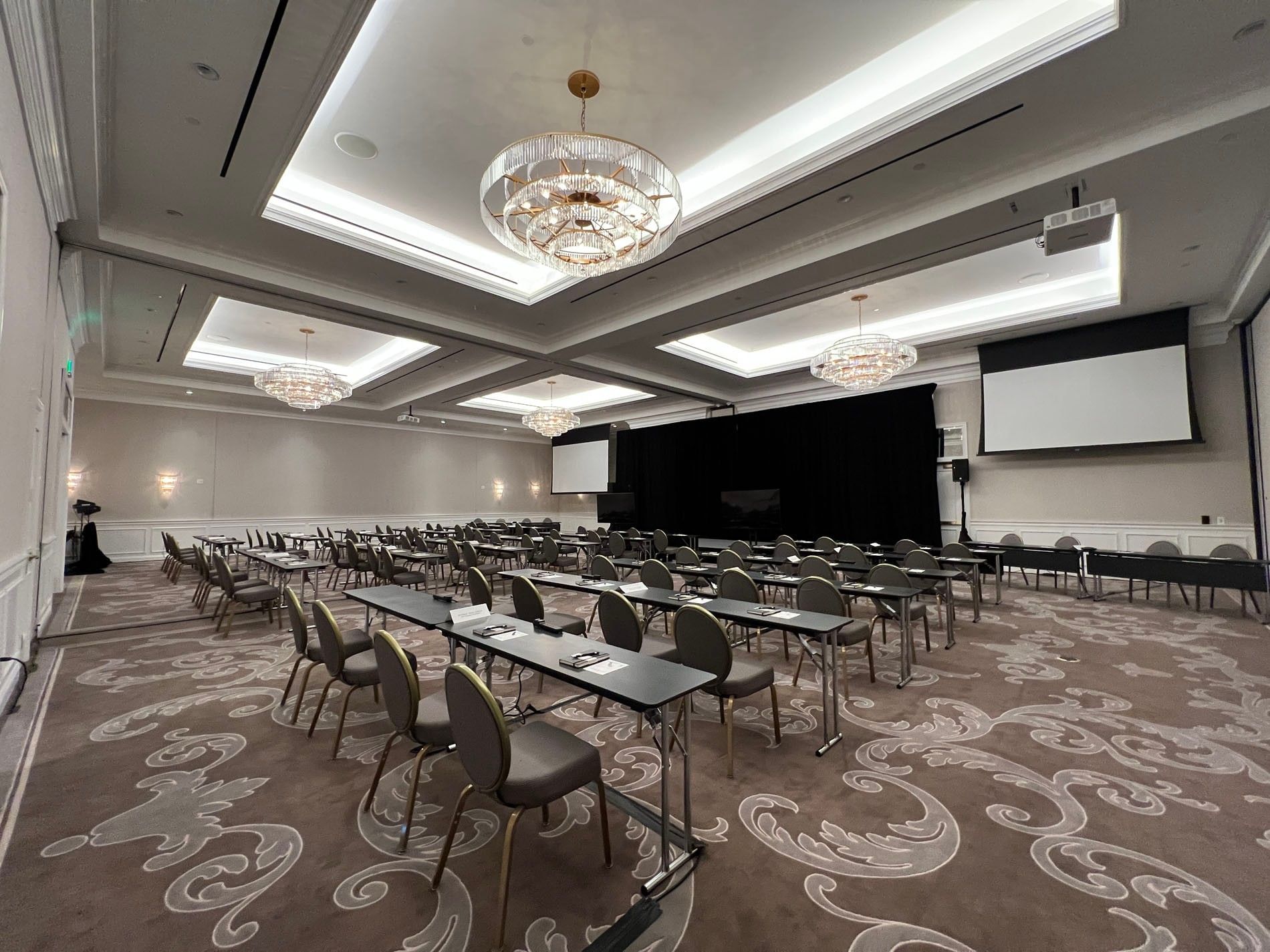 Rows of desks by round-back chairs under tiered crystal chandeliers in Turtle Creek Ballroom B at Warwick Melrose Dallas