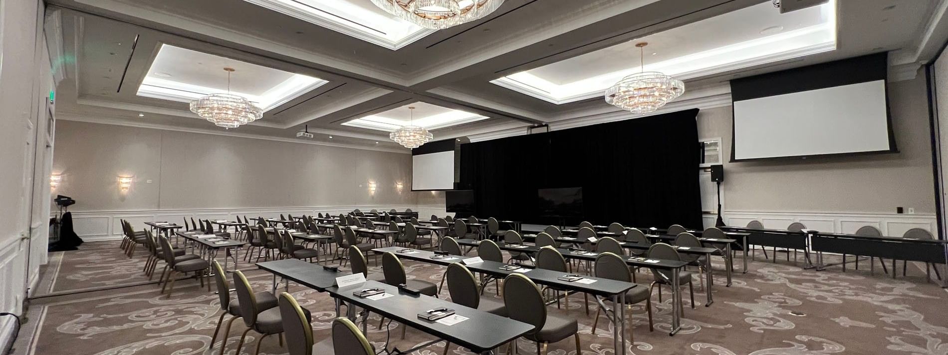 Rows of desks by round-back chairs under tiered crystal chandeliers in Turtle Creek Ballroom A at Warwick Melrose Dallas