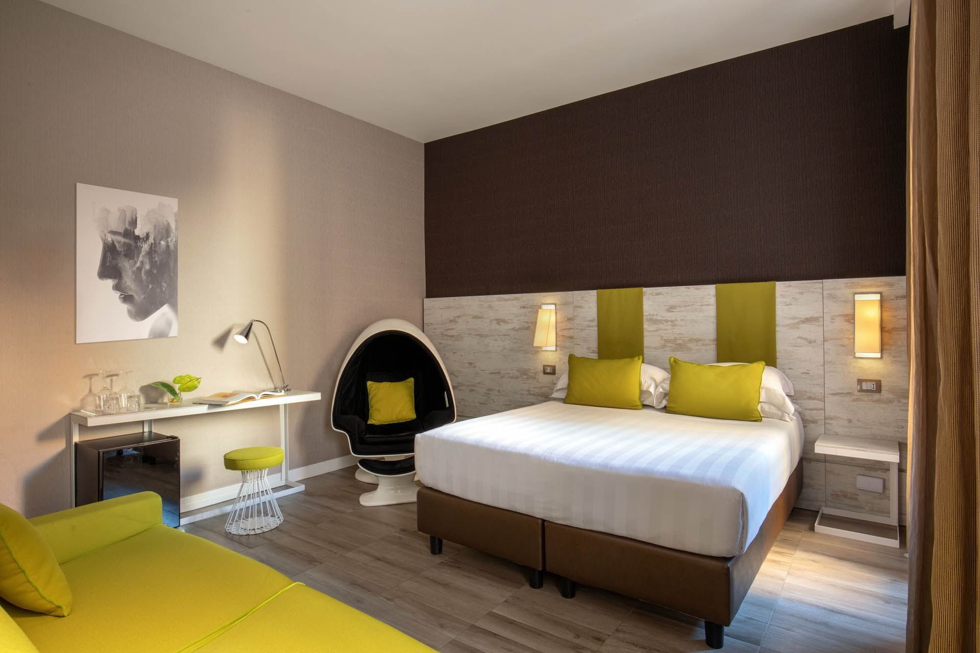 Stylish room at The Guardian Hotel with a cozy bed, yellow sofa, sleek desk, and a stylish egg chair in the corner
