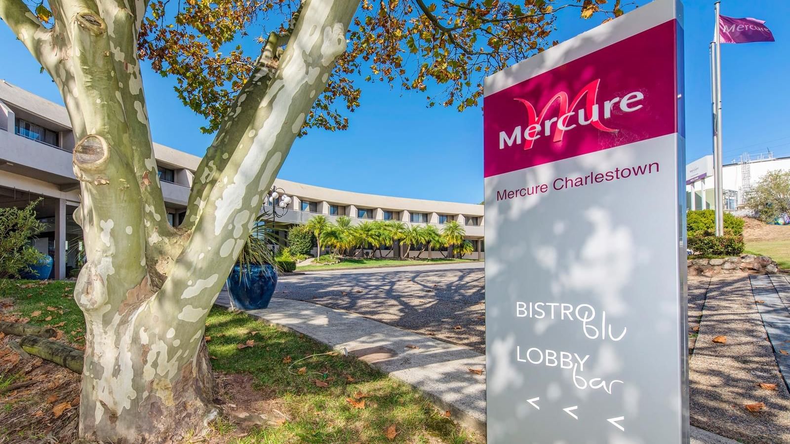 Mercure Charlestown signboard featuring text for Bistro Blu and Lobby Bar, surrounded by greenery at Mercure Charlestown