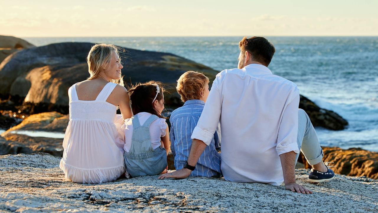 Family of four sitting on rocky beach watching ocean waves