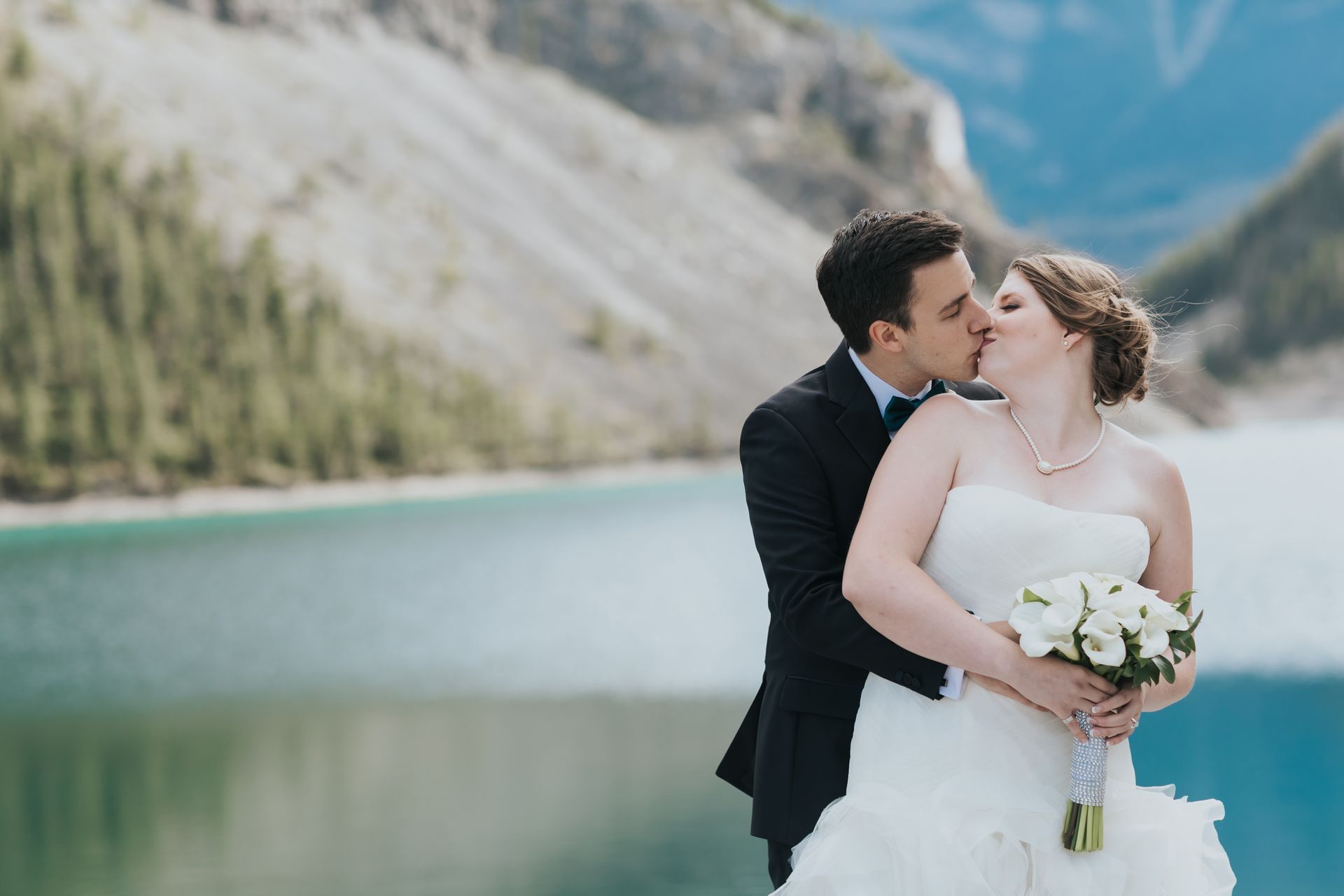 Bride and groom kissing in front of lake and mountains
