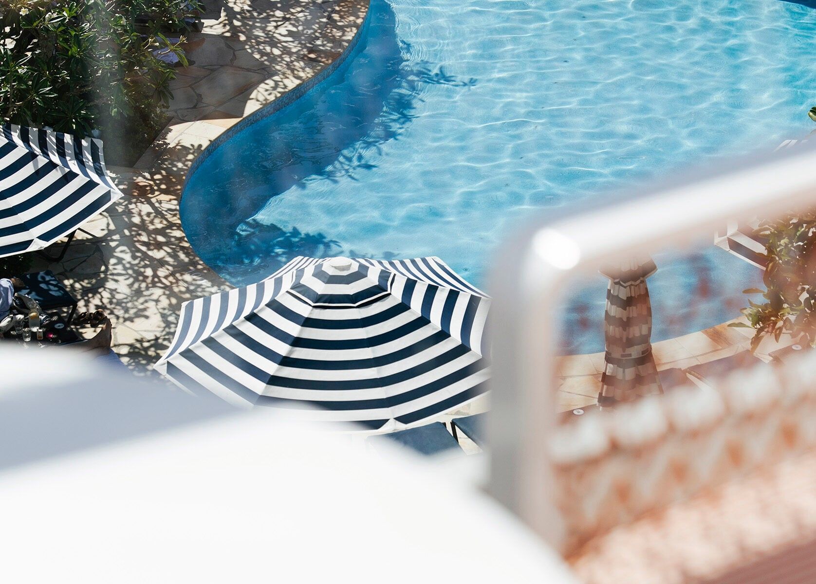 Striped umbrellas by a curved pool, framed by a balcony railing at Elysium Hotels, a featured hotel in Neutral Bay, Sydney