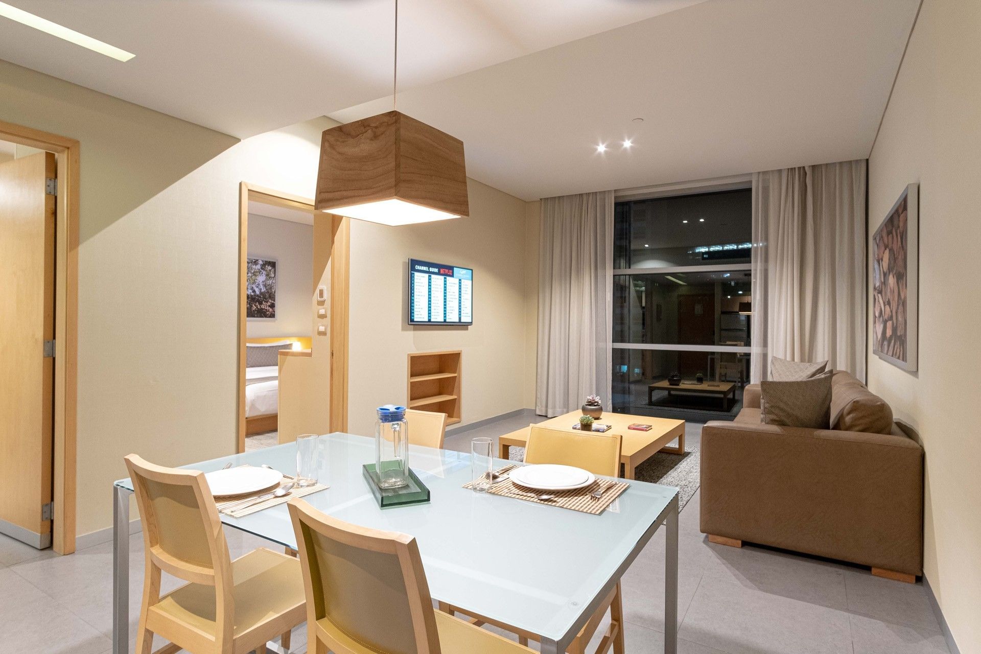 Glass dining table under a wooden pendant light by a living area in Executive Suite 1 King Bed at Stadia Suites Mexico City