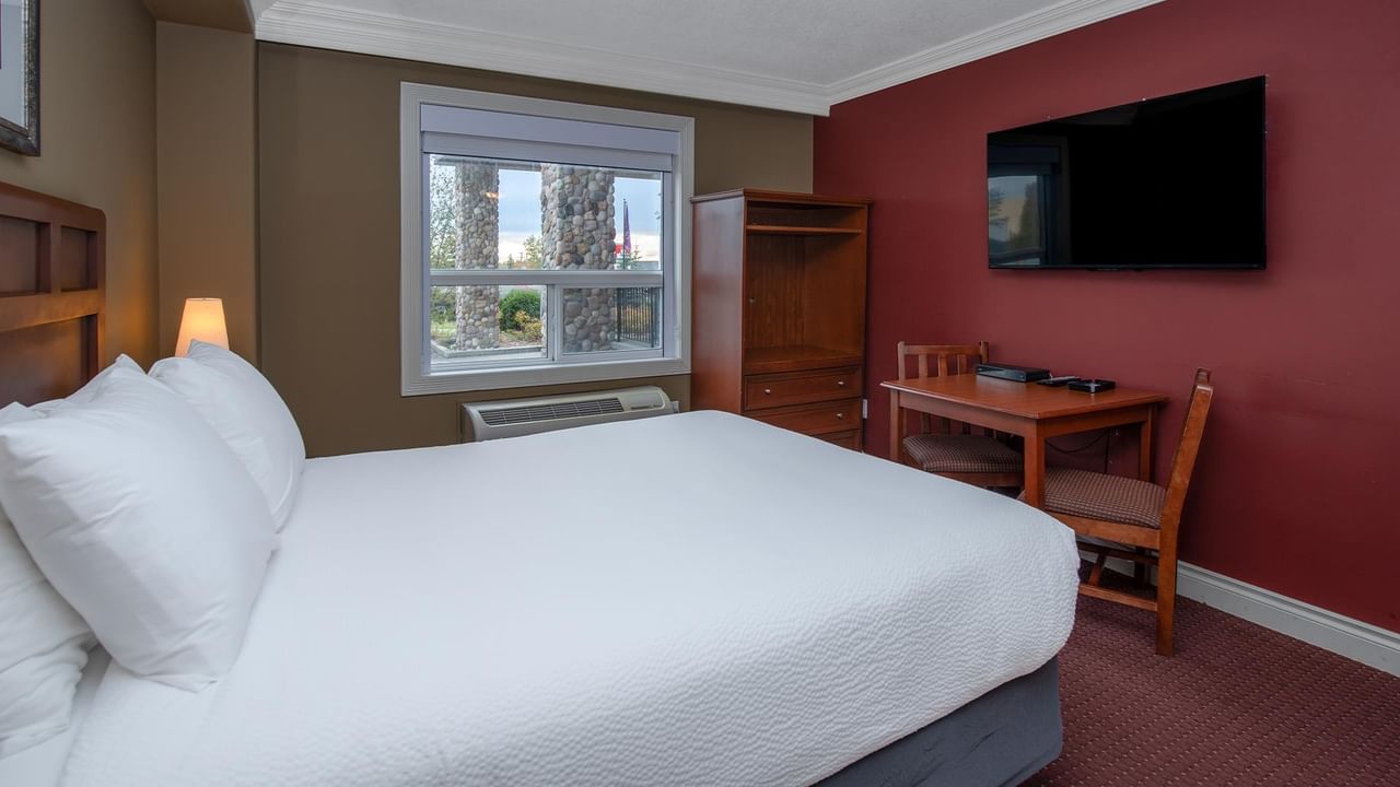 Guest room with white bedding, wooden desk, wall-mounted TV, and red accent wall at Coast Edson Hotel.