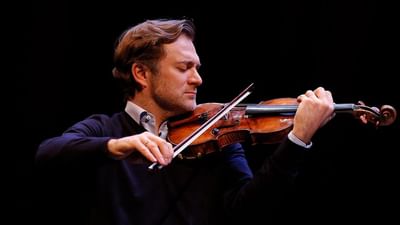 Homme élégant jouant du violon avec un archet, concentré sur sa performance musicale.