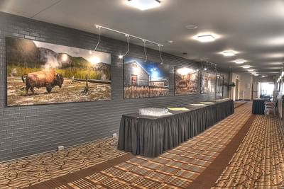 Hallway with large framed artwork depicting Western scenes and long draped tables at Buffalo Bill Village